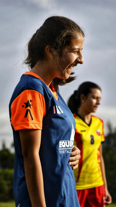 two female soccer players in their uniforms with grass and bushes behind them