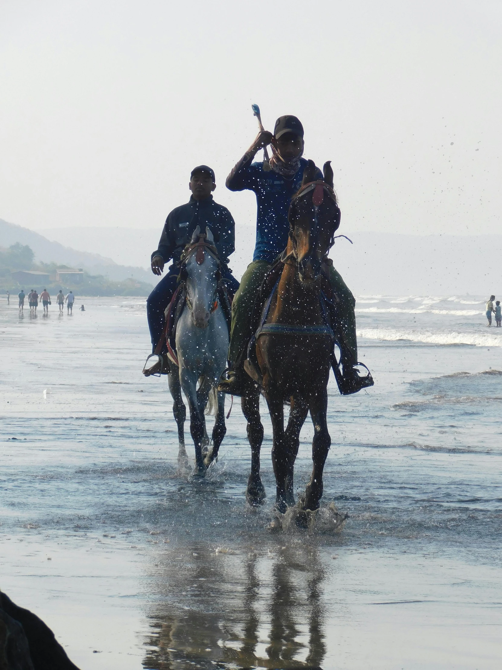 two men riding horses on the beach next to the ocean