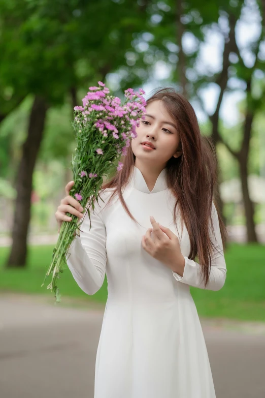 an attractive woman in white dress holding a bunch of flowers