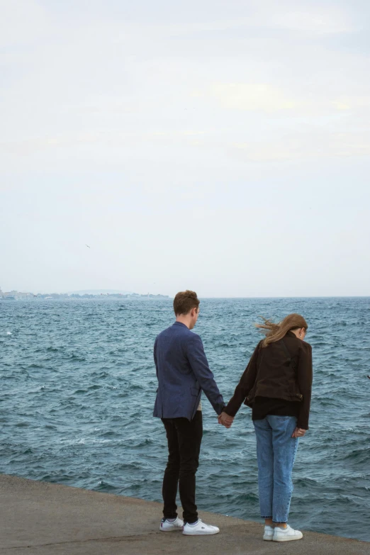 two people holding hands looking out over the water