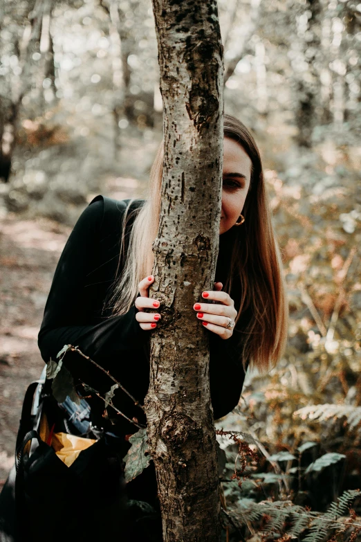 a girl is hiding behind a tree in the woods