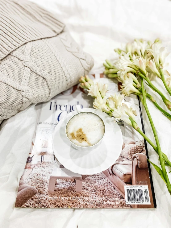 a cup of coffee with a book and some flowers on the bed