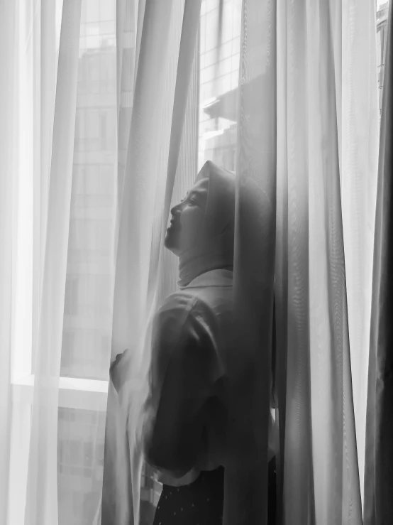 a woman standing next to a window looking out the window