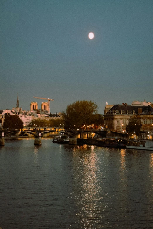 moon over a river with boats floating near it