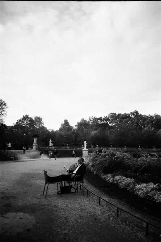 some people sitting at the park and in the distance people are standing around