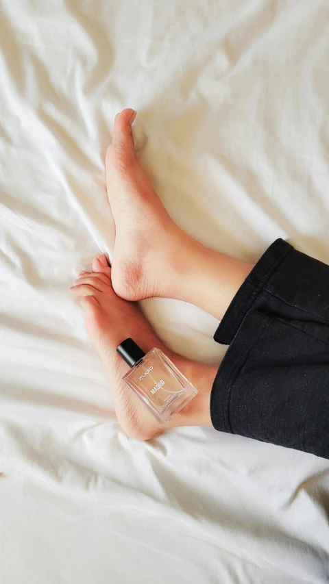 there is someone's feet resting on the bed with a nail polish bottle