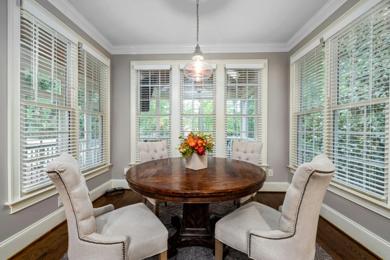 a dining room table with four chairs near two windows