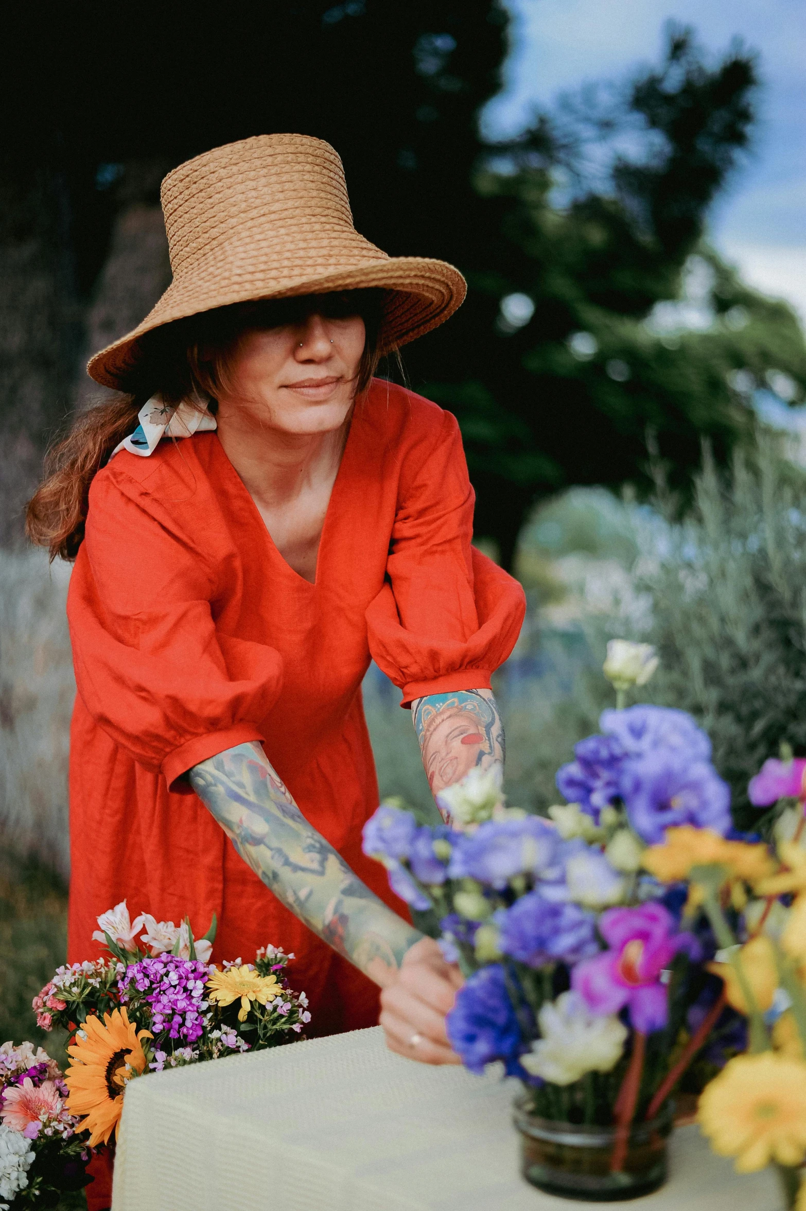 a woman in a large hat is putting flowers into a pot