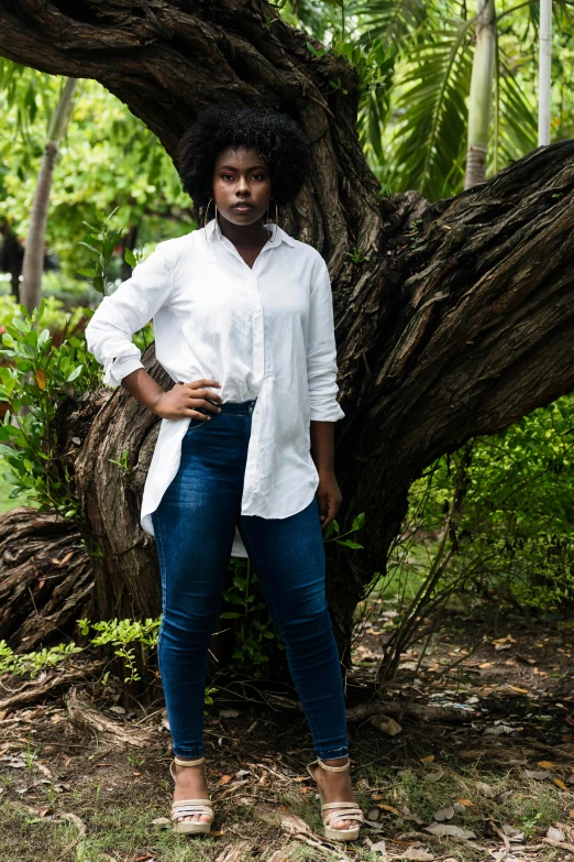 a woman wearing a white shirt standing next to a tree