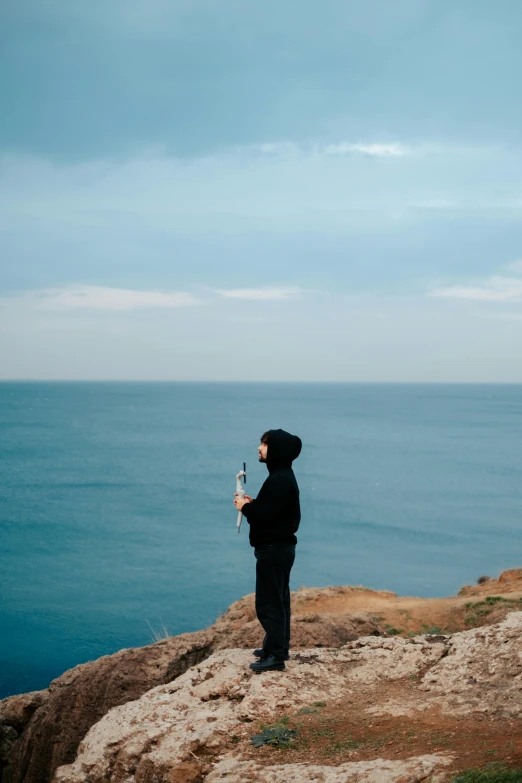 a man holding a bottle while standing on top of a cliff