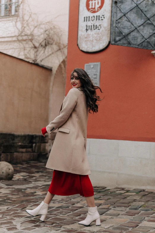 woman in tan coat walking down a brick road