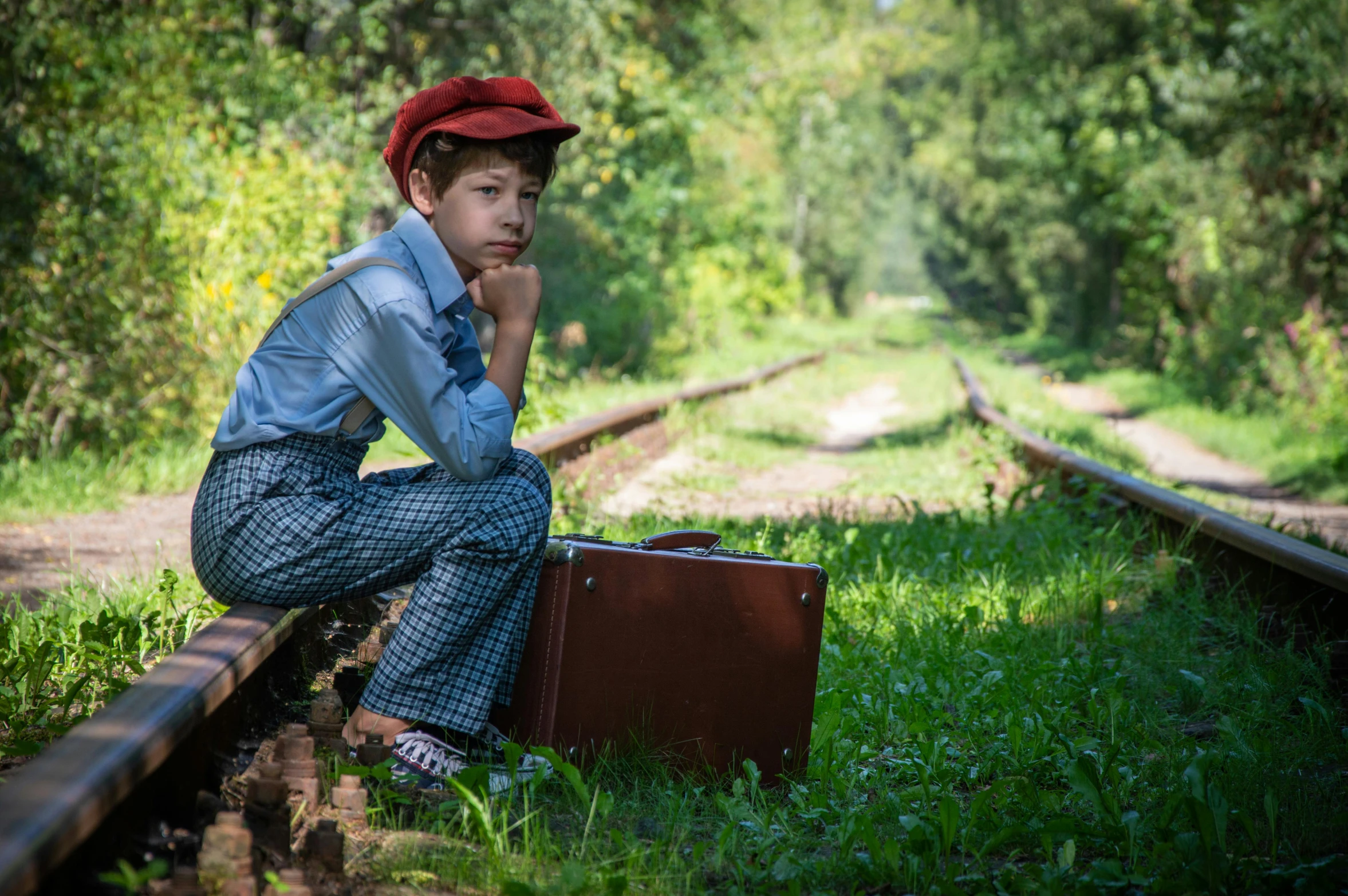 a boy sitting down by a suitcase on the tracks