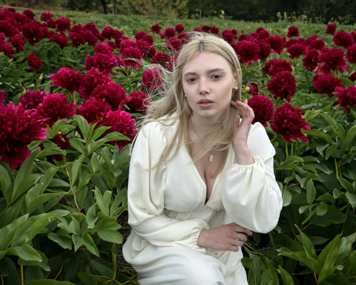 woman wearing white dress sitting in large field of flowers