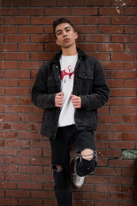 young male in jeans leaning on brick wall