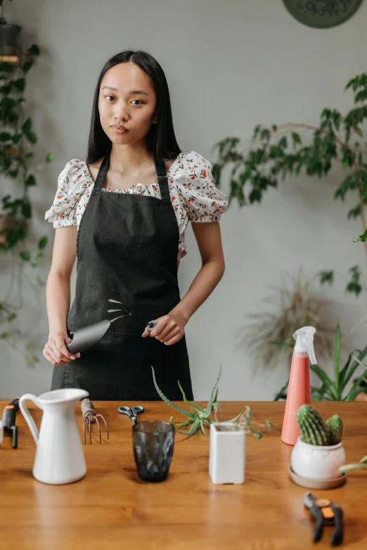 a woman in an apron standing near a table with pots and plant pots