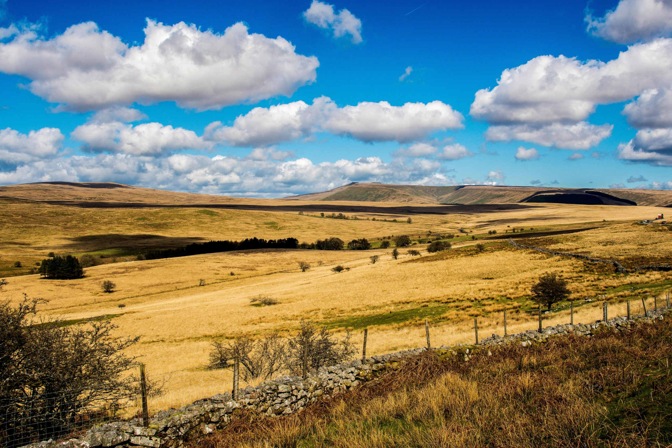 a view of rolling hills and sky, with a fence in the foreground