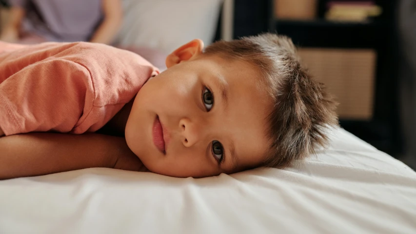 a child lays down on the bed as his mother sleeps in the background