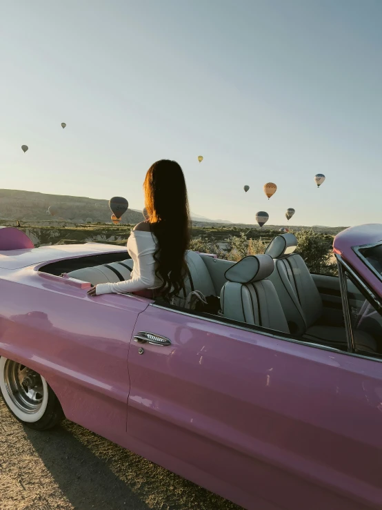 a woman sitting in the passenger seat of a pink convertible