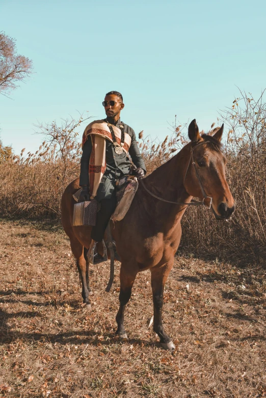 a man riding a brown horse through a dry grass field