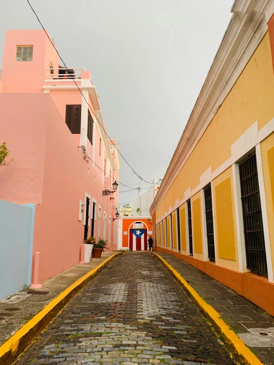 colorful buildings line the street as a man walks on a cobblestone road