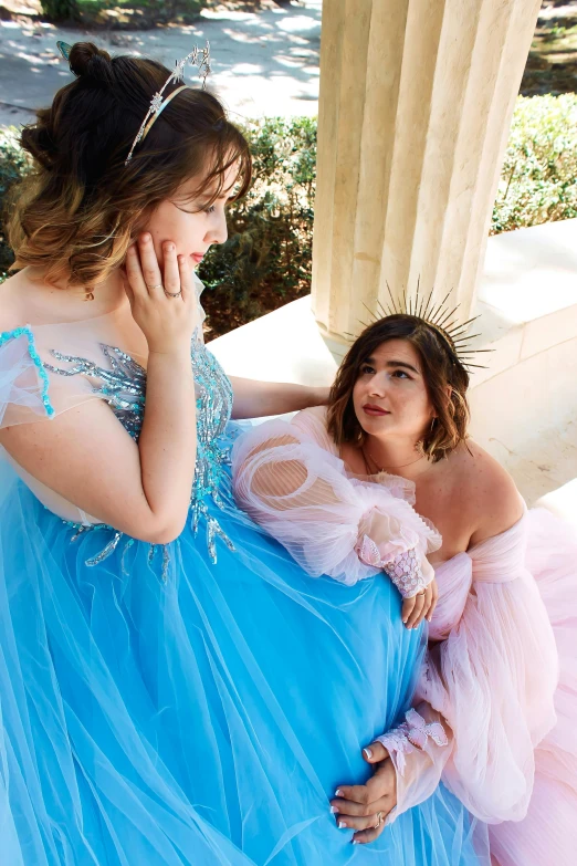 two girls in dresses wearing tiaras talking on a phone