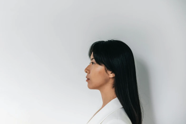 a woman with black hair and a white blazer looking away