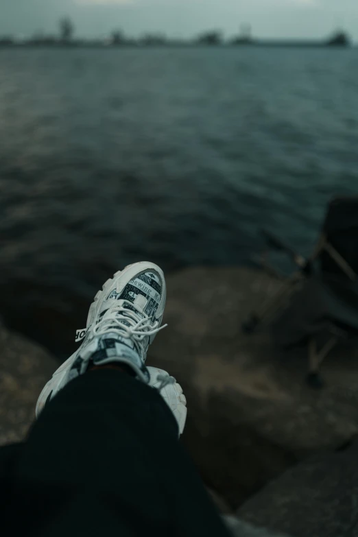 person sitting at the edge of the water with a pair of sneakers