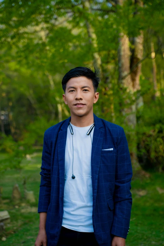 an asian male standing in the middle of a grassy area with trees