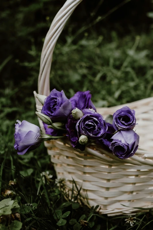 a white basket with purple flowers on top of the grass