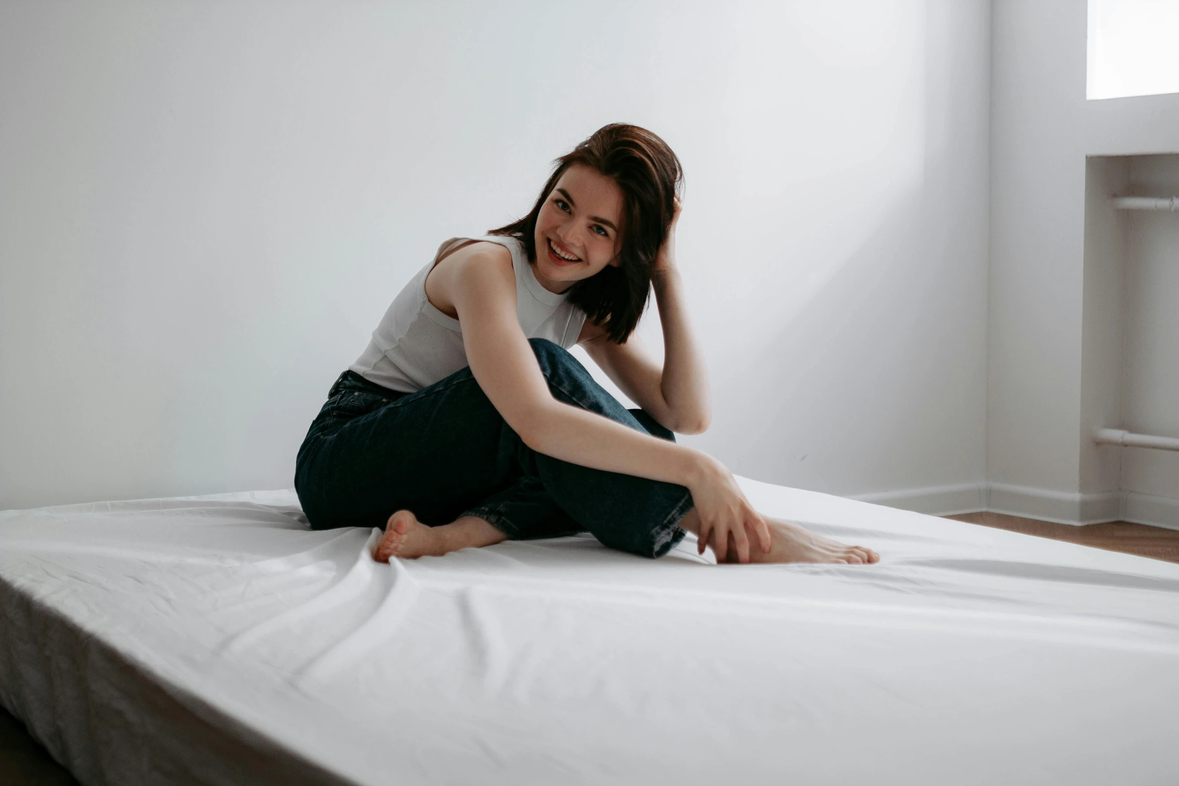 a young woman smiles as she sits on her white mattress