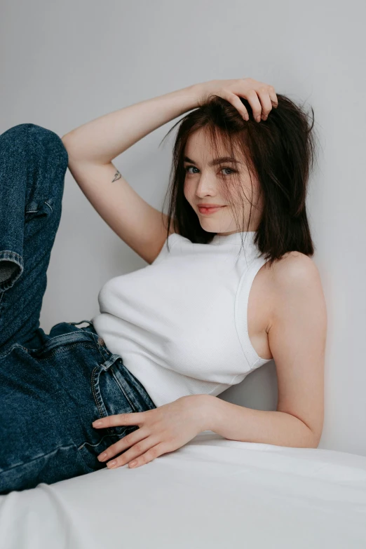 a woman in jeans leaning on her foot while sitting on a bed