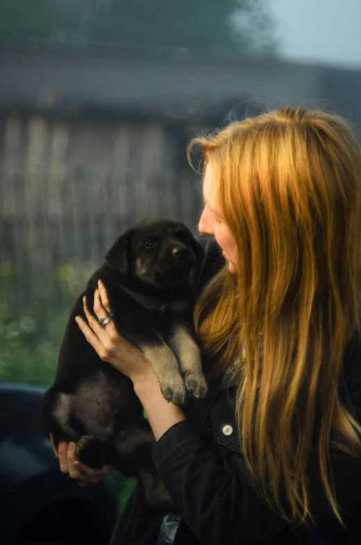 a girl with red hair is holding a black dog