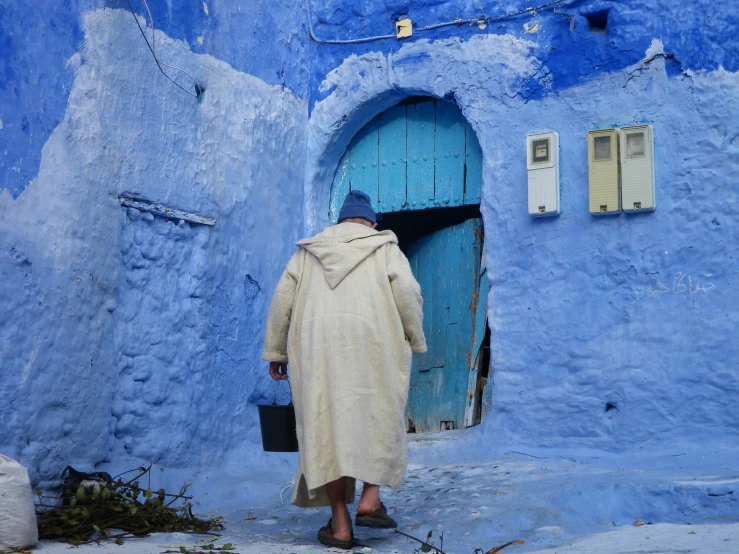 a person in an old coat walking towards an open blue door