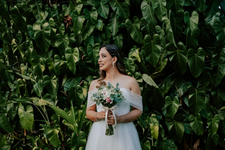 the bride is standing in front of the many greenery