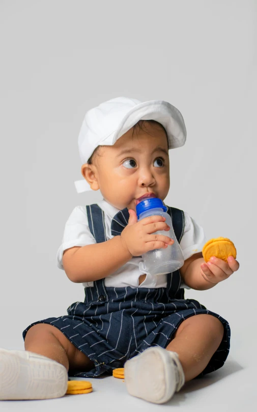 a baby is sitting while drinking a bottle