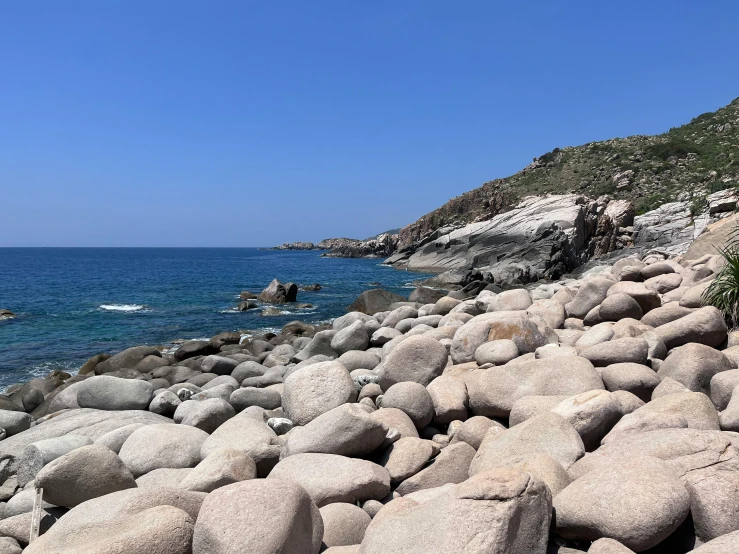 a beach with large rocks, grass and an ocean