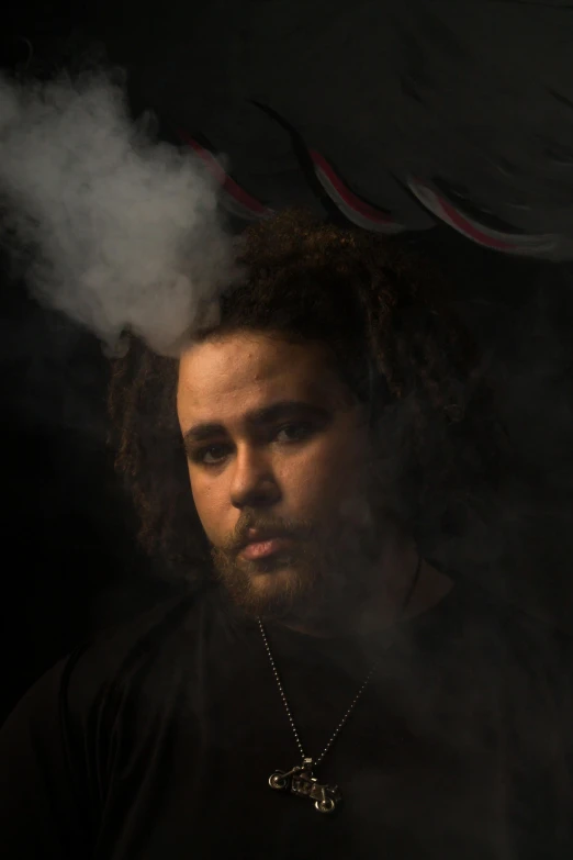 a man with dreadlocks stares ahead while smoke is behind him