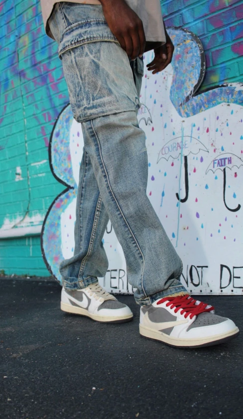 a man standing next to a colorful wall wearing ripped jeans