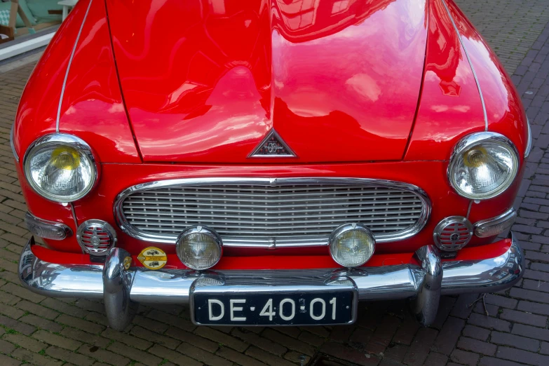 the front end of a red car sitting on a brick road