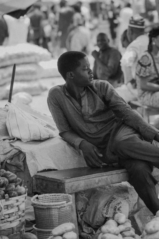 a man sits near various fruits and vegetables on the counter