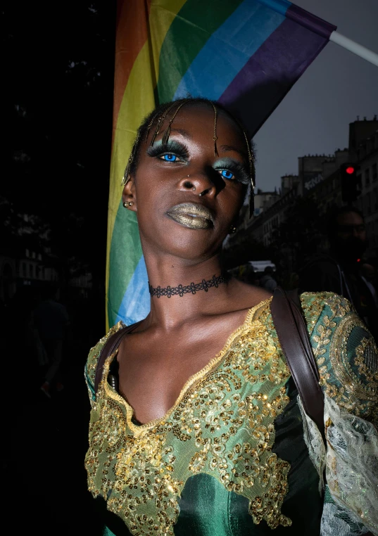 a woman with blue eyes is standing in front of a rainbow flag