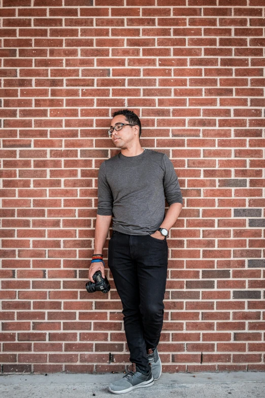 a man with a camera is standing against a brick wall