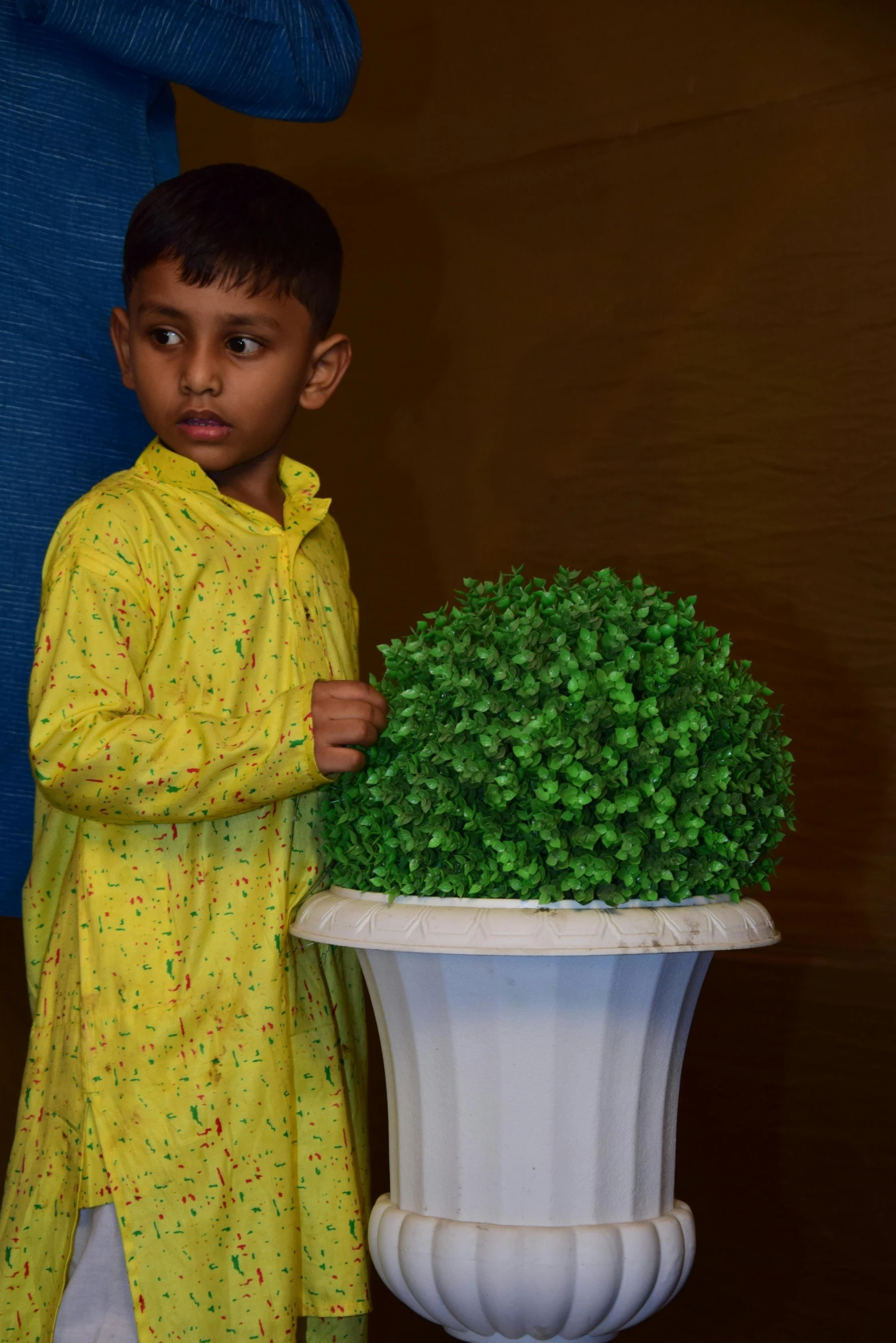 a boy is standing near a potted plant