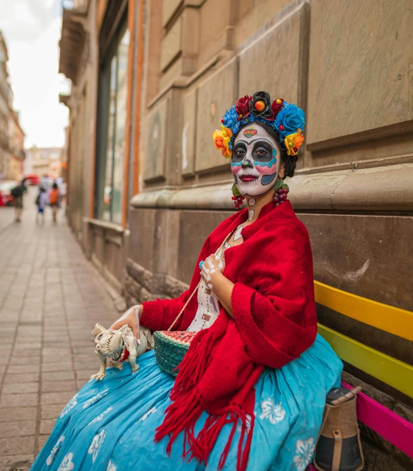 a woman sitting on a street bench wearing a colorful costume and with a bird on it's head