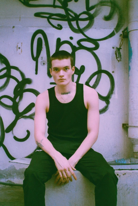 a young man is sitting against a graffiti covered wall