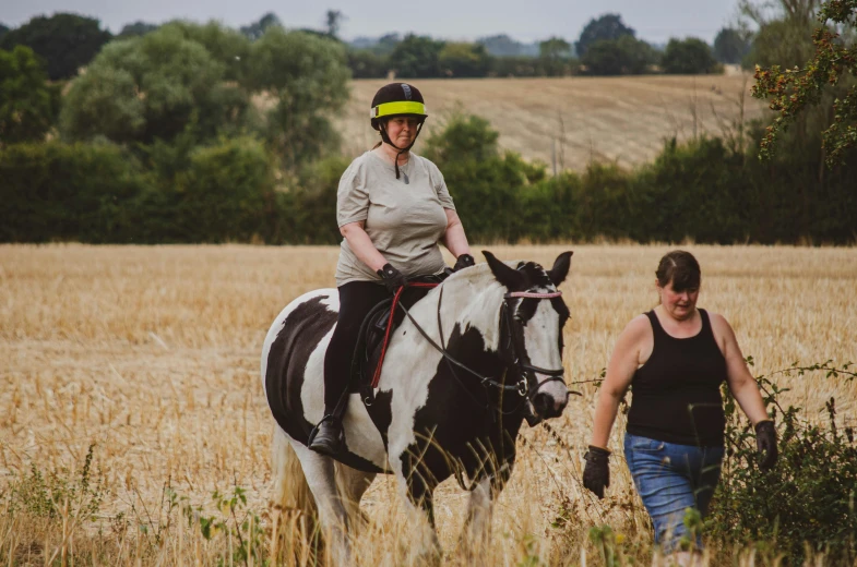 a woman and man wearing helmets ride horses in a field