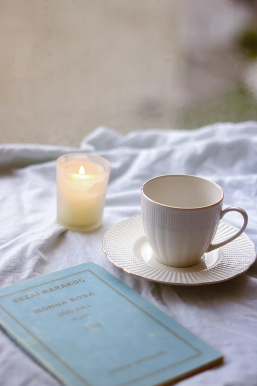 coffee mug with tea cup next to a candle and book