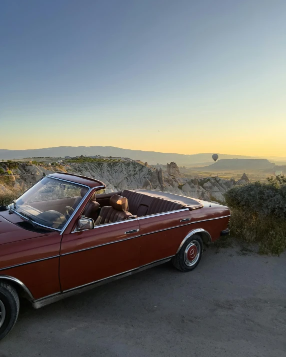 a car with an open hood sits in front of the hills