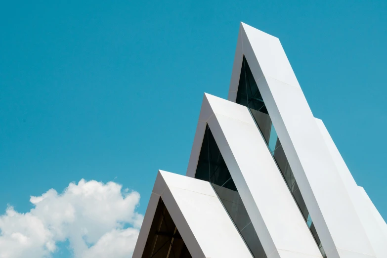 the triangular architectural structure sits on a background of blue sky and clouds