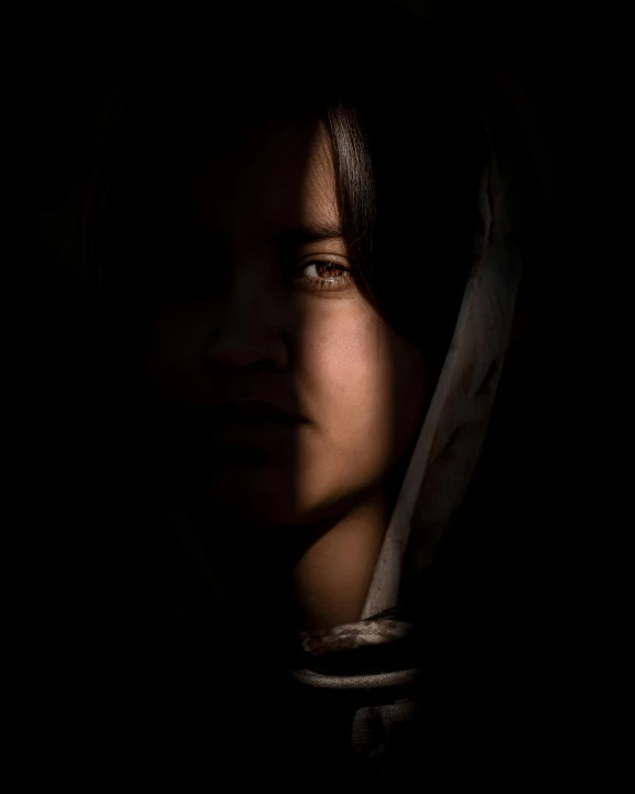 a dark portrait of a 's face with an unkempt hood over her head